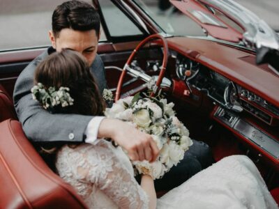 Deux jeunes mariés posent souriants devant leur voiture de mariage décorée